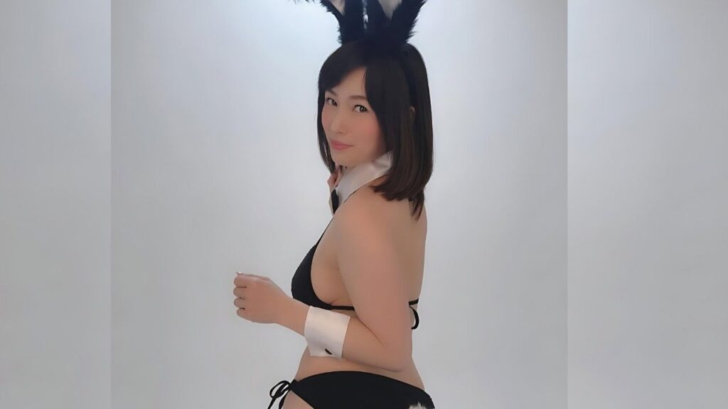 Saki Okuda in a black bunny costume with a white collar and cuffs, tall black ears, short dark hair, smiling softly.