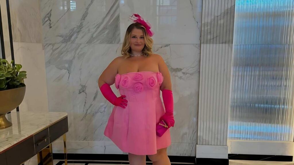 Tiffany Star in a pink strapless dress with rose accents, long pink gloves and clutch, feather headpiece in a marble lobby.