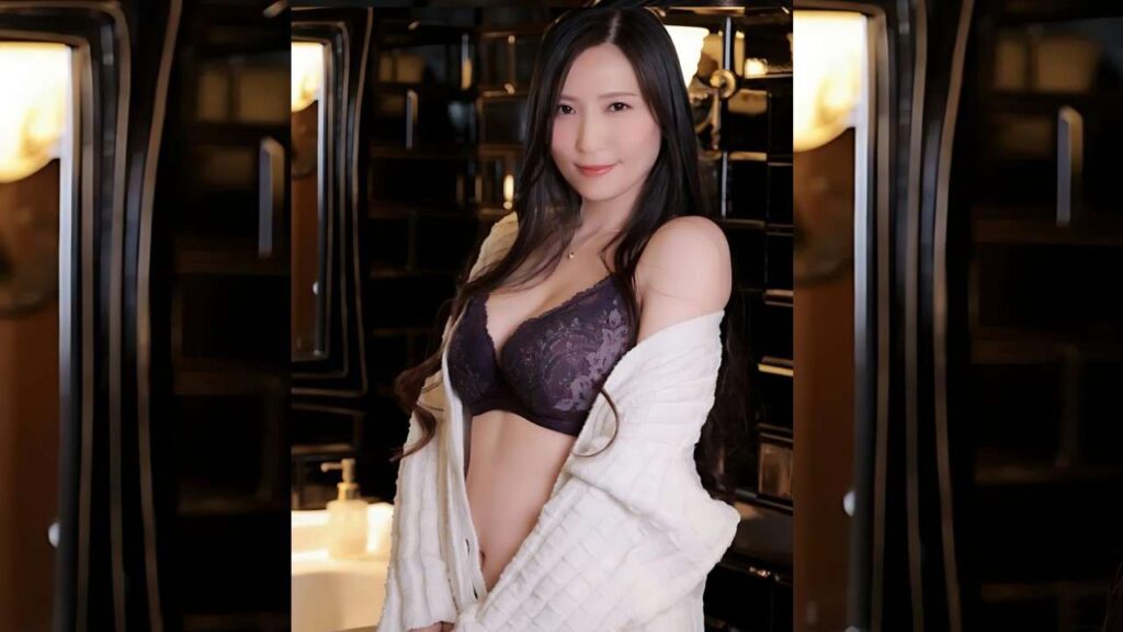 Yuna Shiina (椎名ゆな) in a purple lace bra and white cardigan draped off her shoulders stands in a warm bathroom, smiling softly.