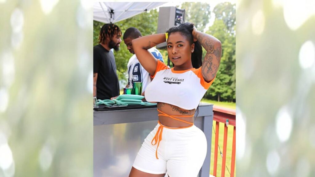 GoGo Zombi in a white-orange cropped top and wrap shorts poses with arms behind her head at an outdoor bar; tattoos visible.