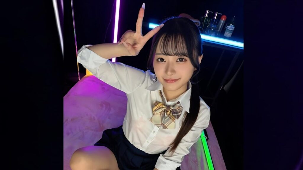 Kaho Hanamori in a white blouse and plaid bow tie sits under neon lights, flashing a peace sign with her right hand.