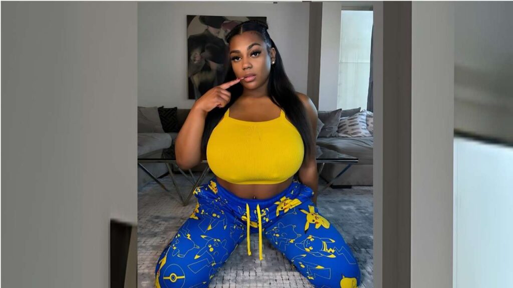 Keira Nicole kneels on a light rug in a living room, wearing a bright yellow crop top and blue Pikachu-patterned pants, finger to lips, long dark hair.