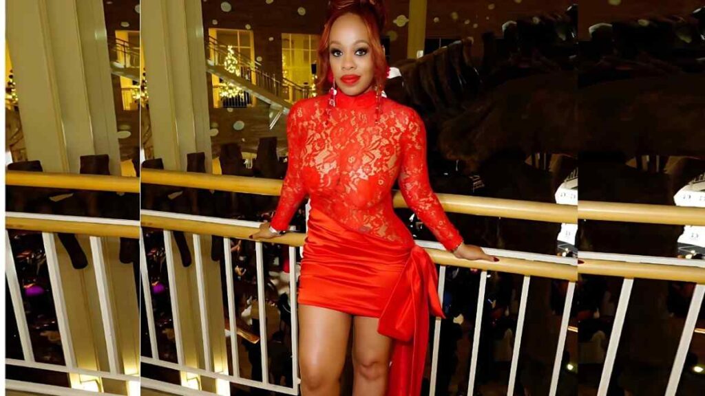 Melrose Foxxx in a red lace top and matching mini skirt leans on a gold-trim balcony railing in a warmly lit venue.