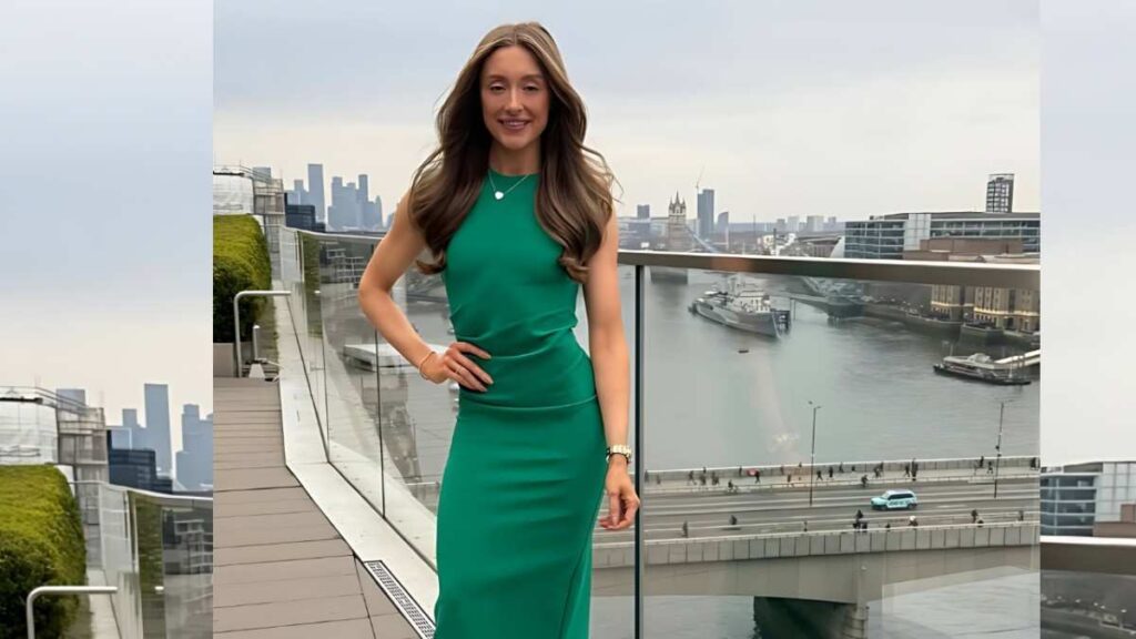 Mia Collins on a glass-railed rooftop, one hand on hip, smiling with river and city skyline behind.