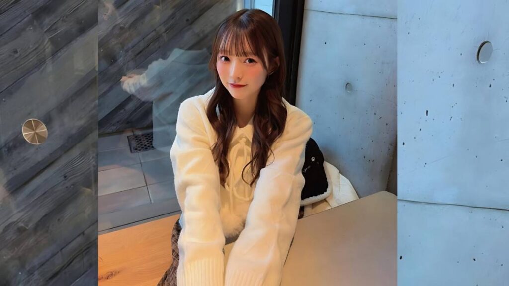 Miyu Umeda with long brown hair and a cream sweater sits at a wooden table, smiling warmly in a modern gray wooden interior.
