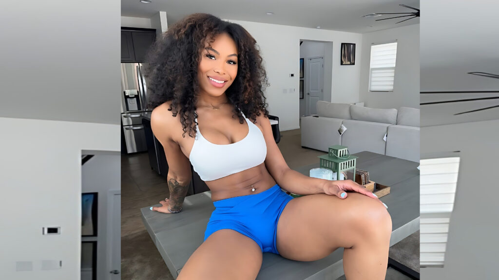 Nadia Jay with curly hair sits on a gray kitchen island in a bright modern home, wearing a white sports bra and blue shorts.