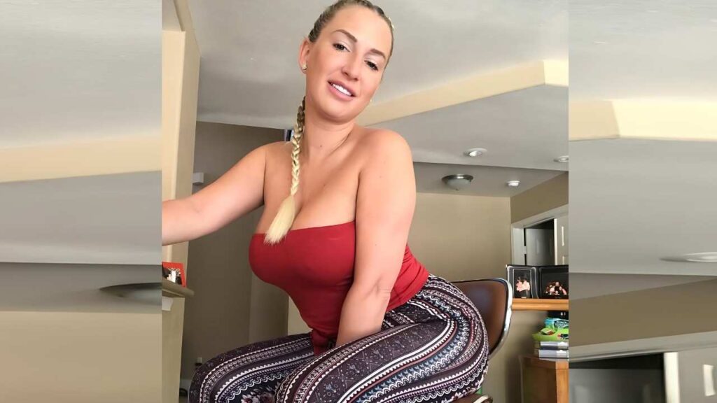 Quinn Waters with a long blonde braid wears a red strapless top and patterned leggings, seated on a chair indoors.