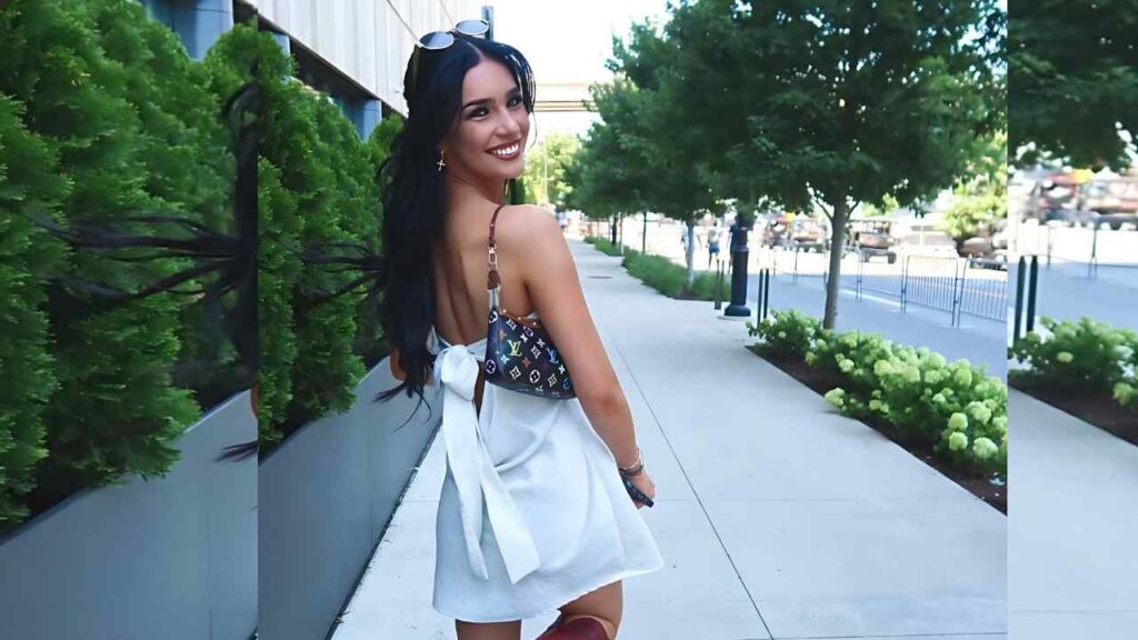 Samantha Ryan glances over her shoulder at the camera while walking on a sidewalk, white halter dress with bow, LV bag.