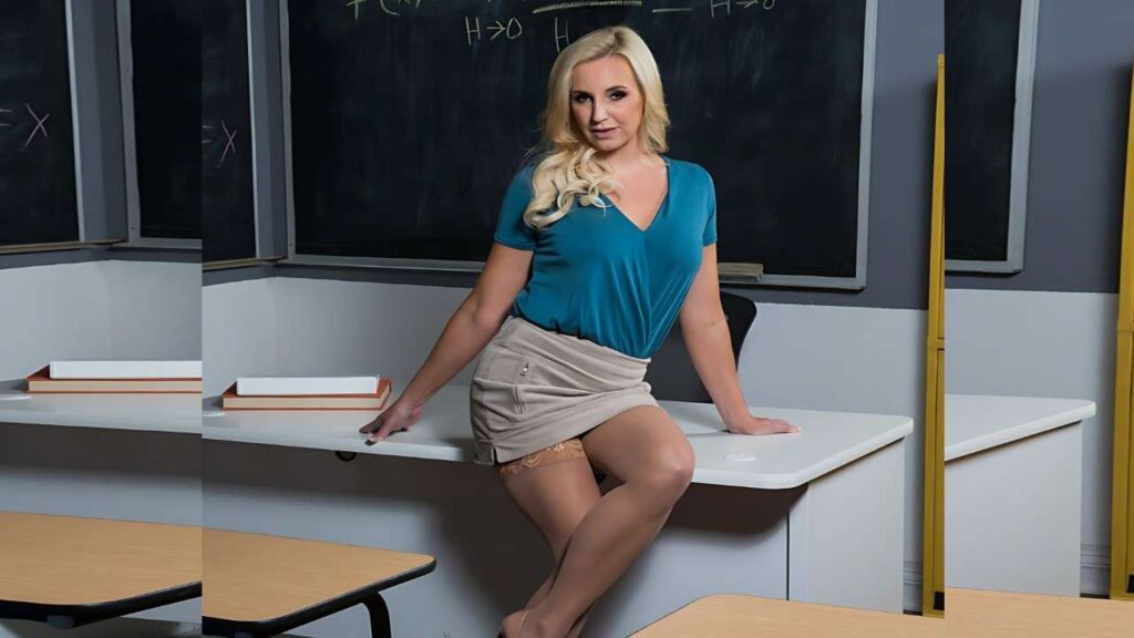 Sophia West in teal V-neck top and beige mini skirt sits on classroom desk, stockings visible, chalkboard behind.