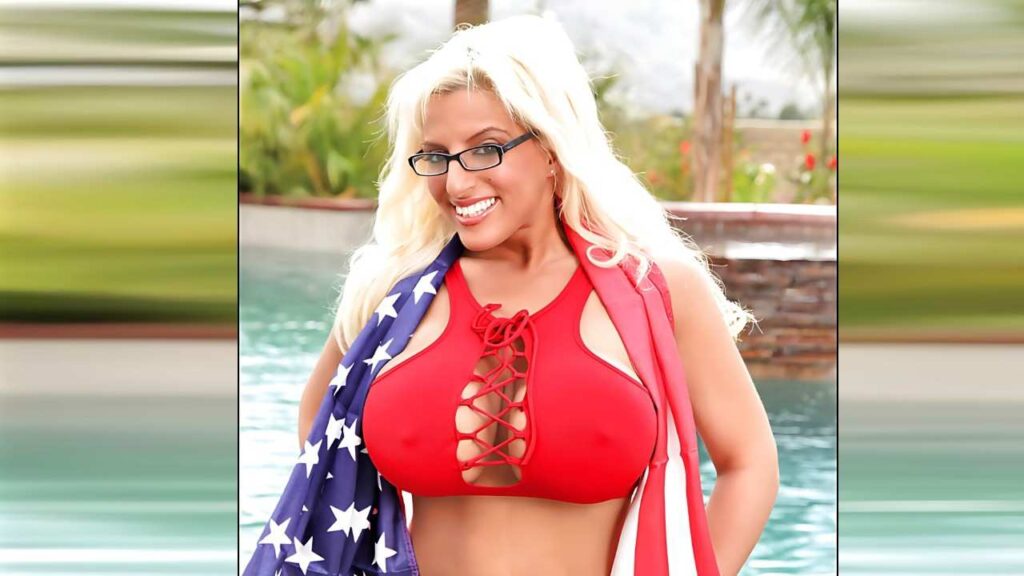 Taylor Stevens with glasses wears a red lace-up bikini top, draped in a flag, by a pool in a sunny backyard.