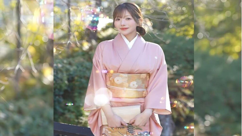 Fujisaki Rina in a pastel pink kimono with a gold floral obi stands in a sunlit garden, holding a cream clutch and smiling softly as bubbles drift.