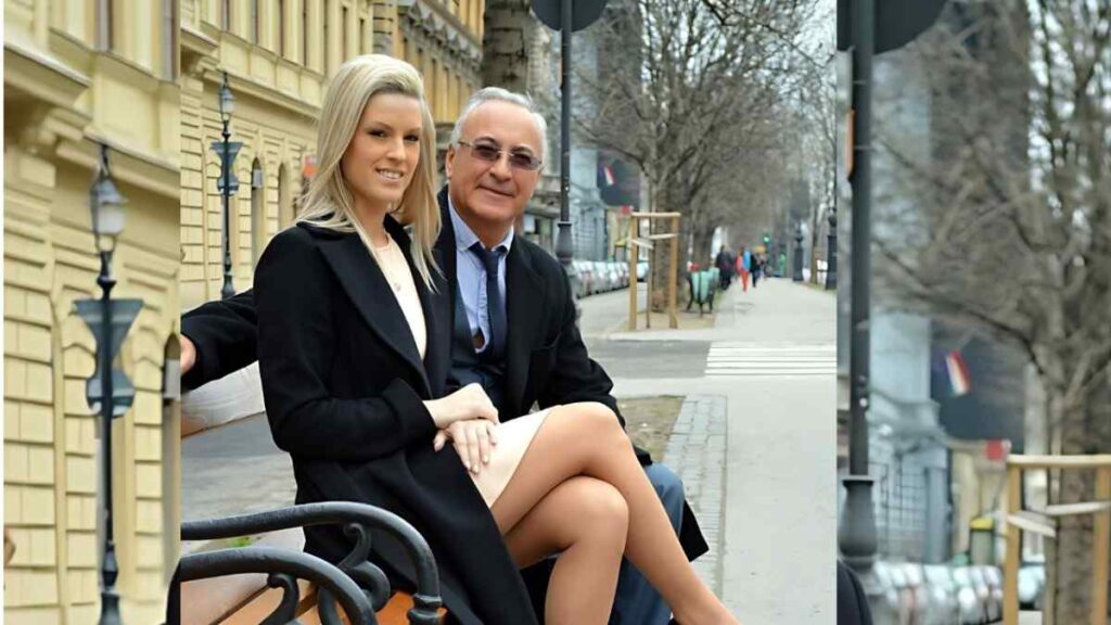 Jim Slip in a suit on a bench by a yellow brick building.