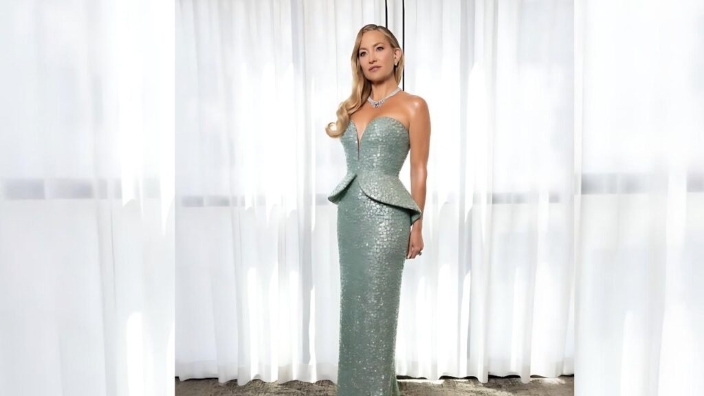 Kate Hudson in a mint-green sequined strapless gown with a peplum waist, diamond necklace, posing near sheer white curtains