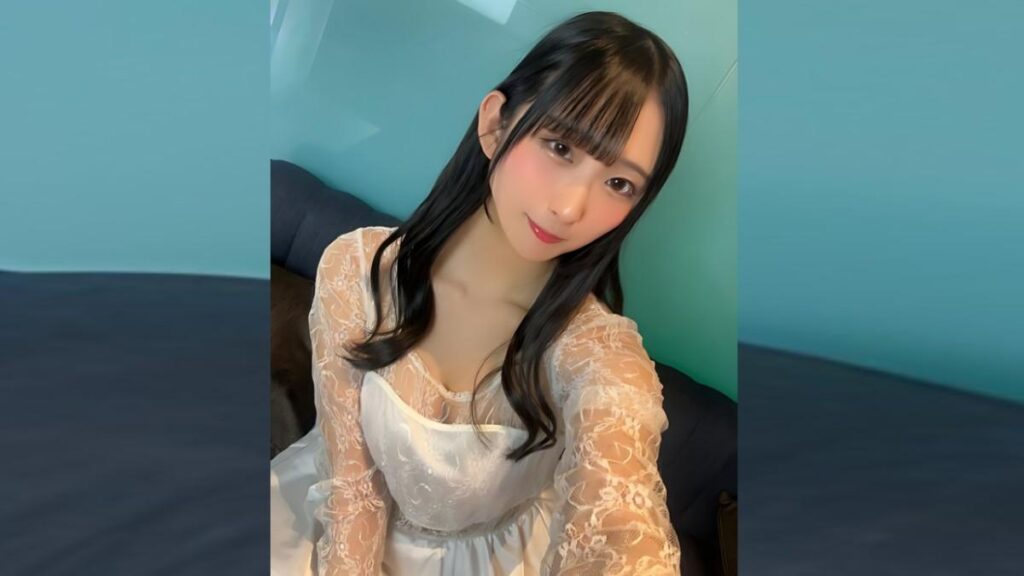 Marina Yakuno with long black hair and bangs sits on a couch, wearing a white lace dress, against teal walls, smiling softly.