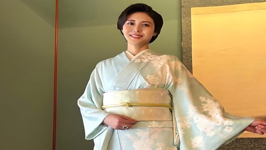 Matsushima Nanako in a pale blue floral kimono with cream obi, standing beside a green wall and beige screen.