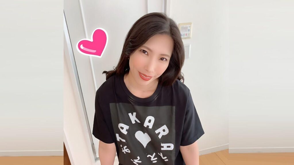 Miki Yamase with dark hair in a black tee with a heart and circular letters; pink heart sticker nearby.