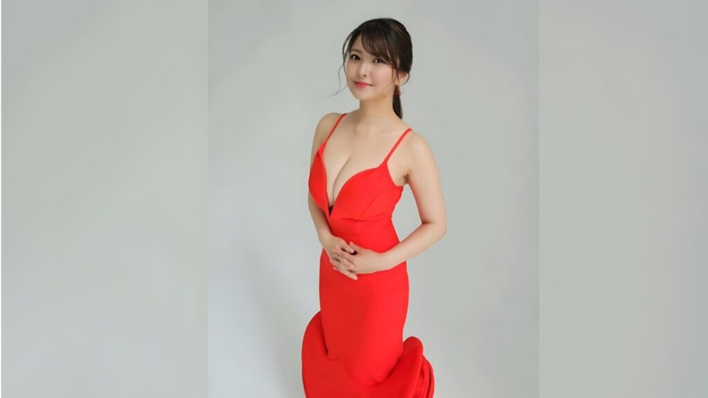 Miri Hanai in a red spaghetti-strap dress with a plunging neckline, standing against a pale gray backdrop, smiling softly.