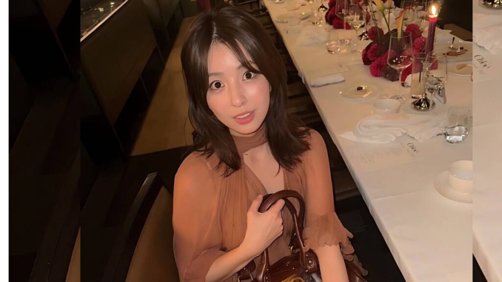 Yurina Yanagi with shoulder-length brown hair in a peach sheer blouse sits at a candlelit dining table, holding a handbag.