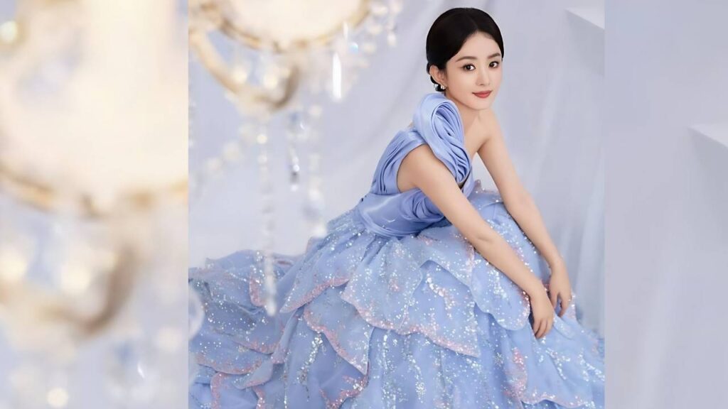 Zhao Liying in a sky-blue, voluminous sequined tulle ball gown sits with hands on her lap, hair in a neat updo, against a soft pastel backdrop.