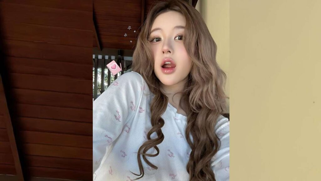 Zhao Lusi with long wavy brown hair and pink makeup poses indoors in a light patterned top, with a playful, open-mouth expression.