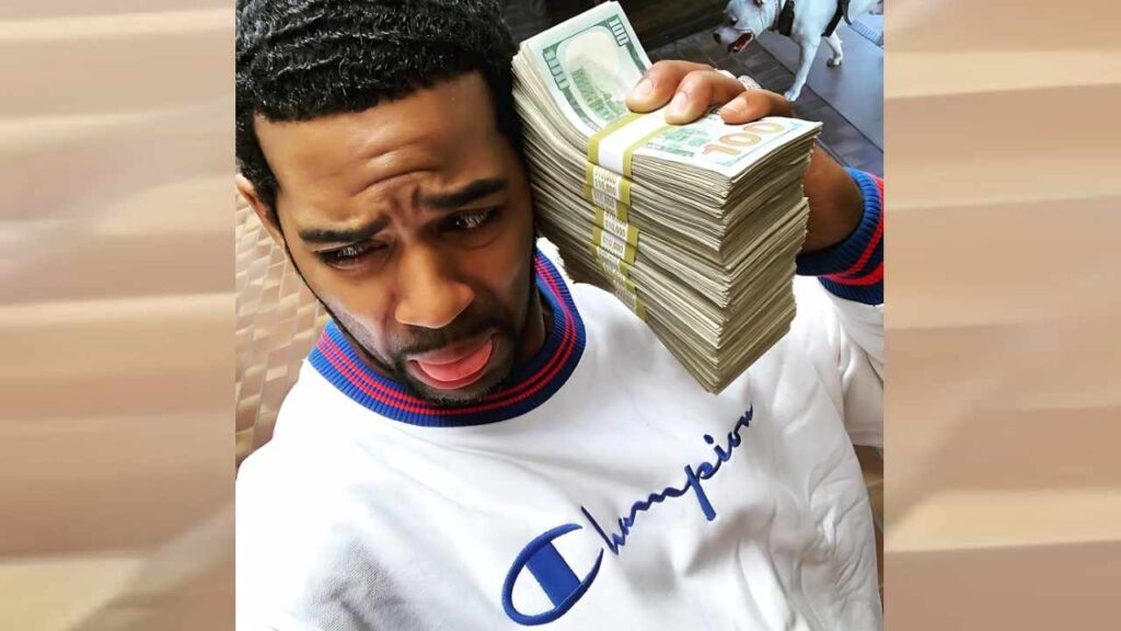 Brian Pumper in a white Champion sweatshirt with blue-red trim, a huge stack of $100 bills on his shoulder, sticking out his tongue.