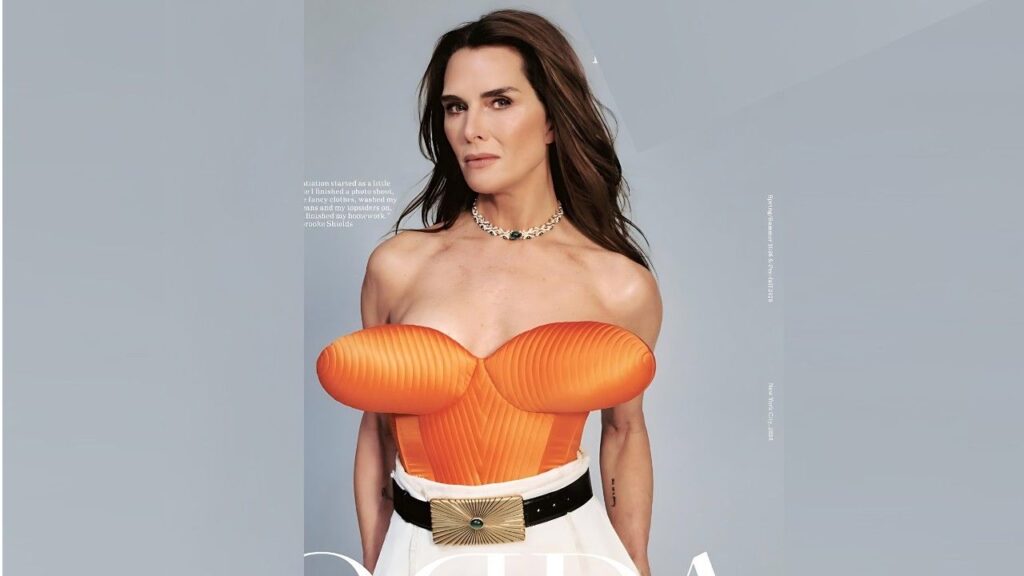 Brooke Shields Orange strapless corset with ribbed cups, white high-waisted skirt, black belt with gold sunburst buckle, gray backdrop.
