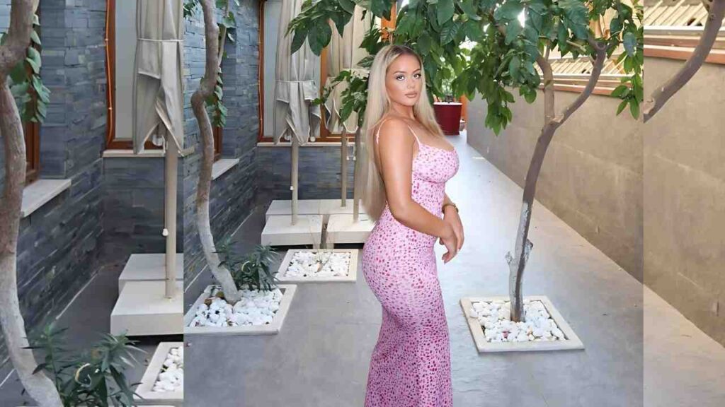 Chloe Nicole in a pink leopard-print halter dress poses in a modern courtyard with potted trees, white pebble planters, and slate stone walls.