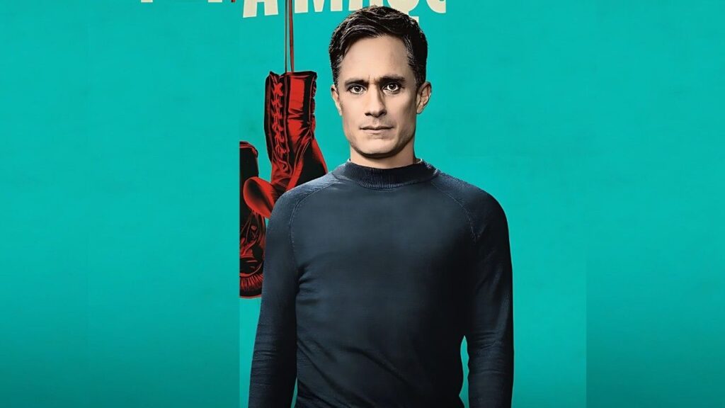 Gael García Bernal in a fitted black long-sleeve shirt stands before a teal background; a red boot hangs behind him, with partial white text above.