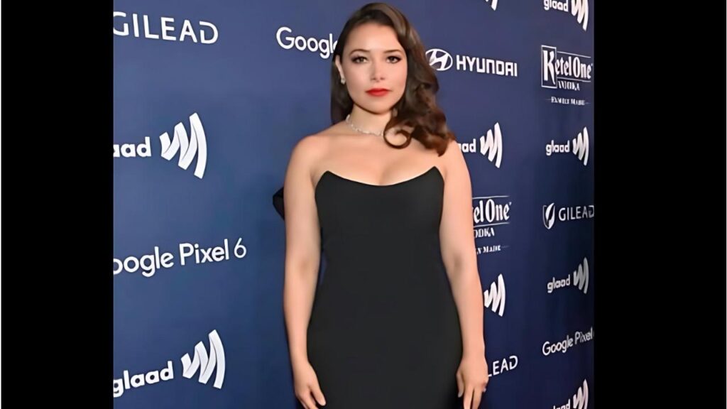 Jessica Parker Kennedy in a black strapless gown poses on a blue step-and-repeat, logos for Google Pixel 6 and GLAAD visible behind her.
