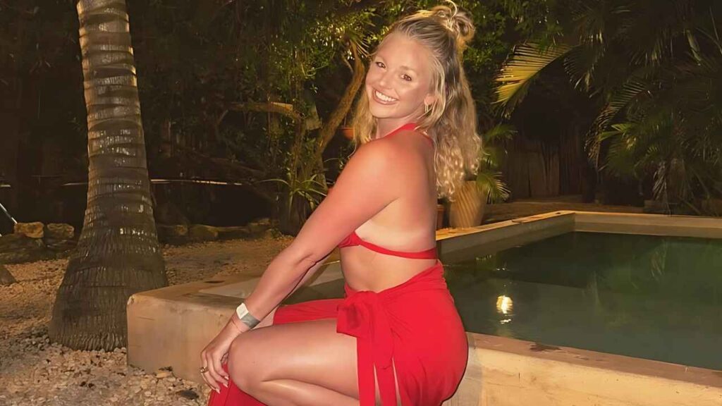 Lauren Lee in a red halter top and wrap skirt sits on the pool edge at night, surrounded by palm trees.