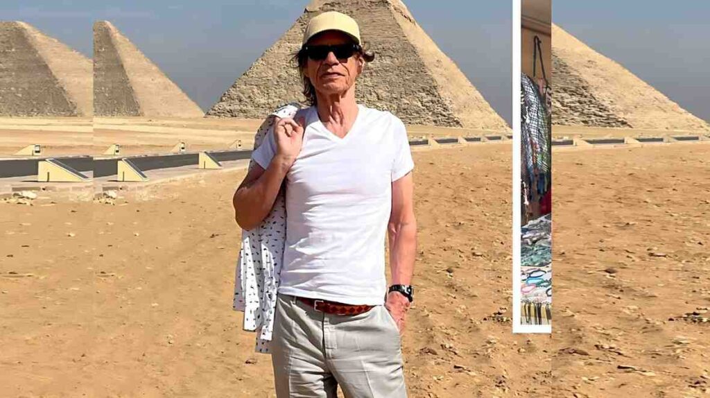 Mick Jagger in a white shirt, beige cap and sunglasses stands before the pyramids, with a patterned jacket slung over his shoulder.