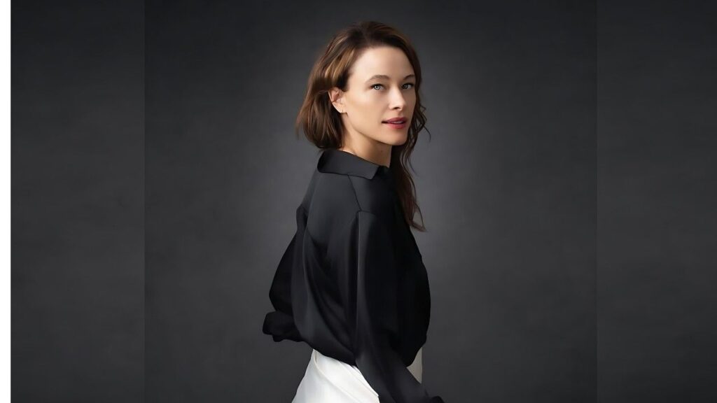 Scottie Thompson in a black satin blouse with loose sleeves, turned slightly left against a dark gray studio backdrop.