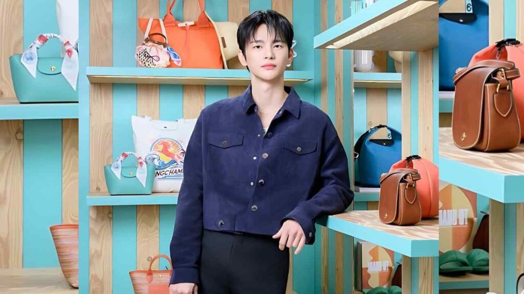 Seo In-guk in a navy jacket stands in a retail display of teal shelves filled with colorful handbags, posing confidently.