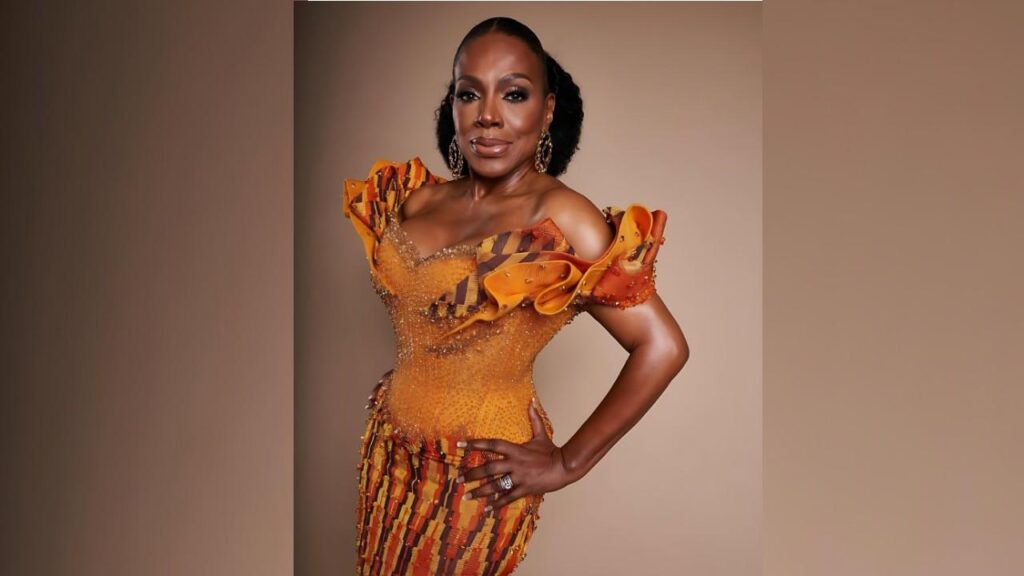 Sheryl Lee Ralph in an orange off-shoulder gown with ruffled sleeves and beaded bodice, posing against a warm beige backdrop.