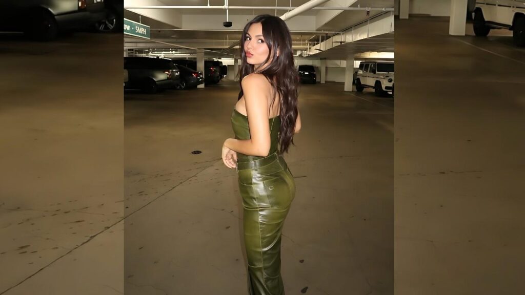 Victoria Justice in olive-green latex outfit poses in a parking garage, turning back over her shoulder with long dark hair.