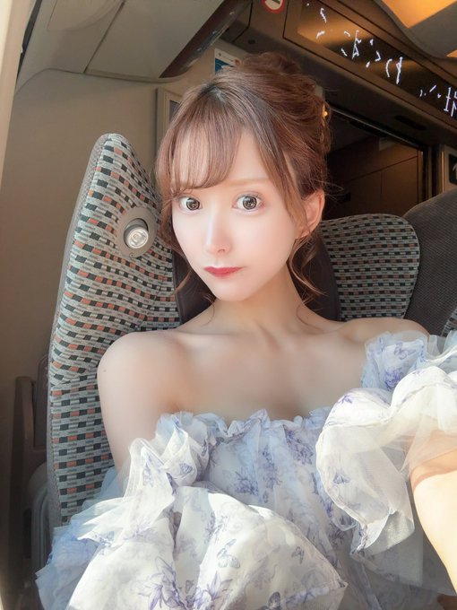 藤井 蘭々 前髪のある女性が、柄入りのグレーの電車の座席に座り、肩出しのラベンダー色の花柄ドレスを着て、柔らかな雰囲気の自撮り写真を撮っている。