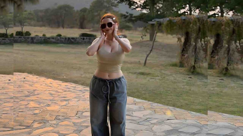 Arleth Rubio in beige tank top and gray pants, wearing sunglasses, stands on a stone patio with grass and trees behind.