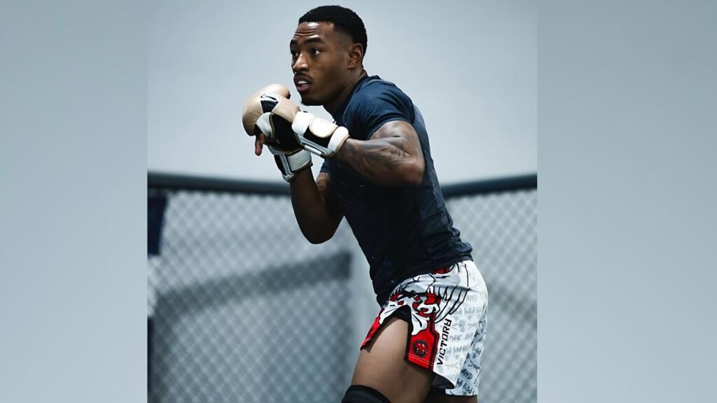 Elijah Smith martial artist in a dark blue athletic shirt and patterned shorts, gloves up in a guarded stance inside a cage.