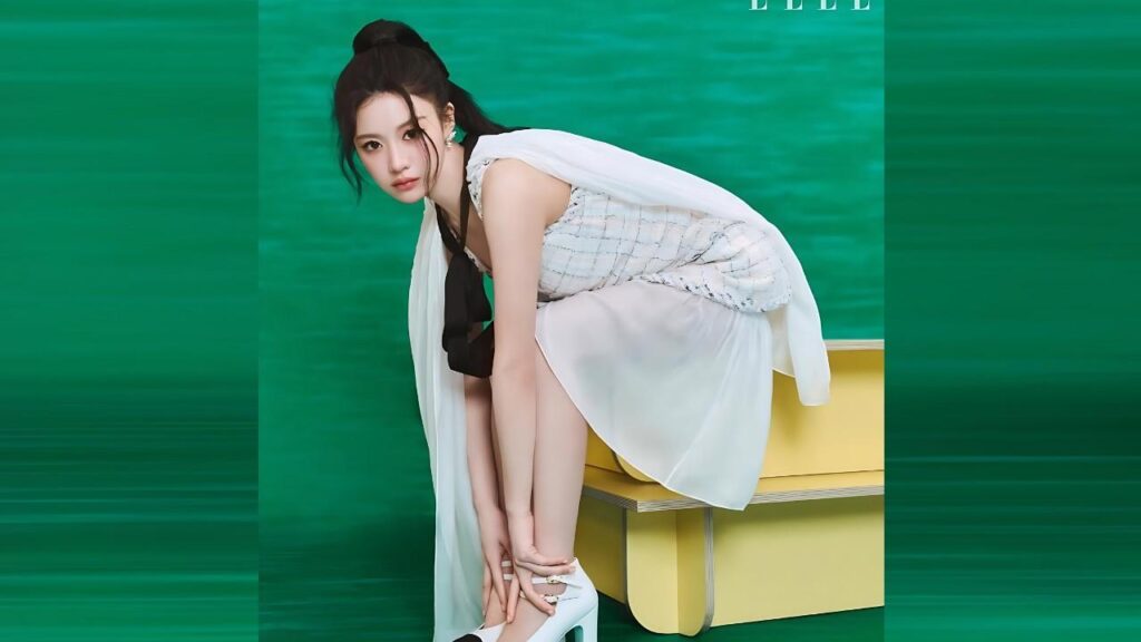 Go Hyun-jung in a pale checkered top and white skirt, bending to touch white heels on a yellow bench before a green backdrop.