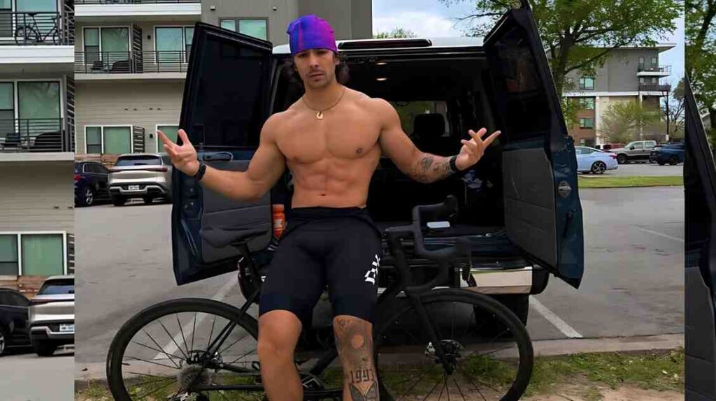 Ian Fonz with purple bandana and necklace stands beside a bike by a van with open rear doors in a parking lot.