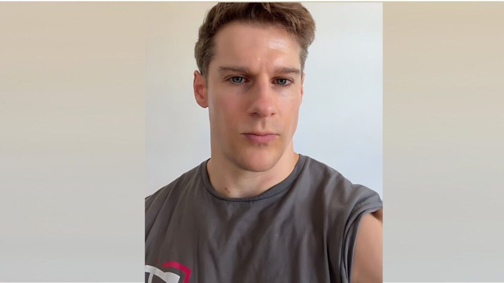 Joel Twinem with short light-brown hair and a gray rolled-sleeve T-shirt, gazing with a serious expression.