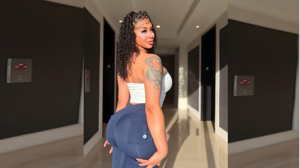 Kayla Otto in a sleek hallway glances back, white bandeau top and blue high-waisted pants, floral shoulder tattoo.