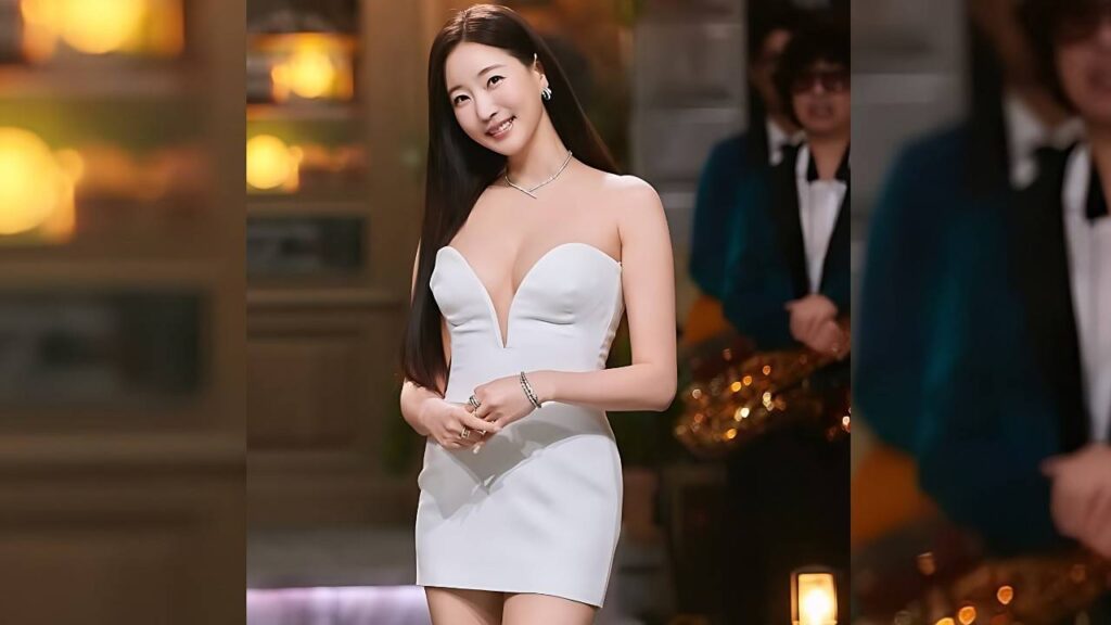 Kim Sa-rang in a white strapless mini dress with long dark hair stands indoors at an event, wearing jewelry.