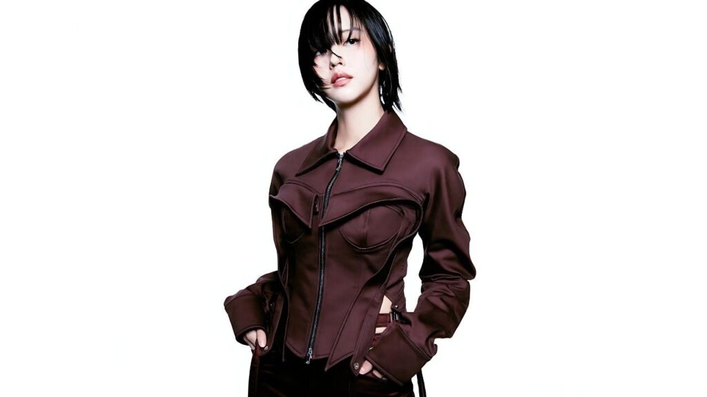 Kim So-hyun in a burgundy structured zip-front jacket with sculpted panels, hands in pockets, fringe across her face against a white background.