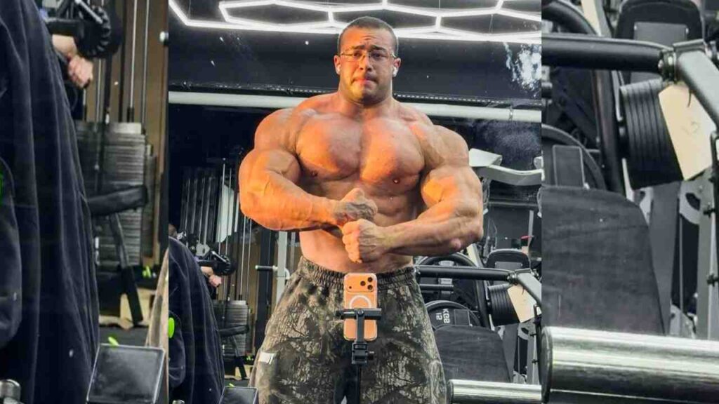 Svein Falzon shirtless, flexing in a gym mirror, camo shorts; orange phone mounted on a stand in front.