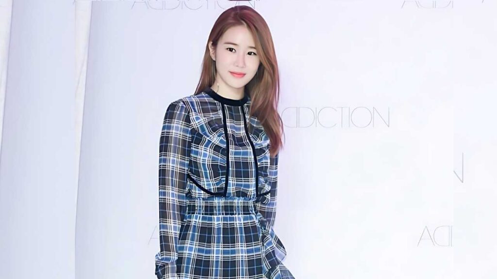 Yoo In-na with long auburn hair wearing a blue plaid dress with black trim, posing against a pale backdrop.