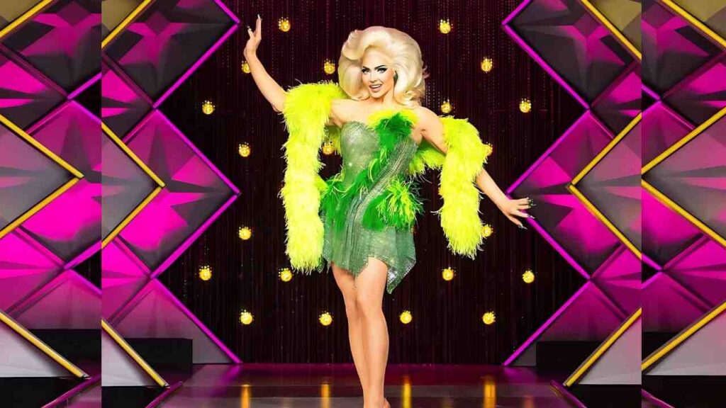 Alyssa Edwards in a glittery green mini dress with neon yellow feather boa, striking a pose on a pink-gold stage, blonde hair.
