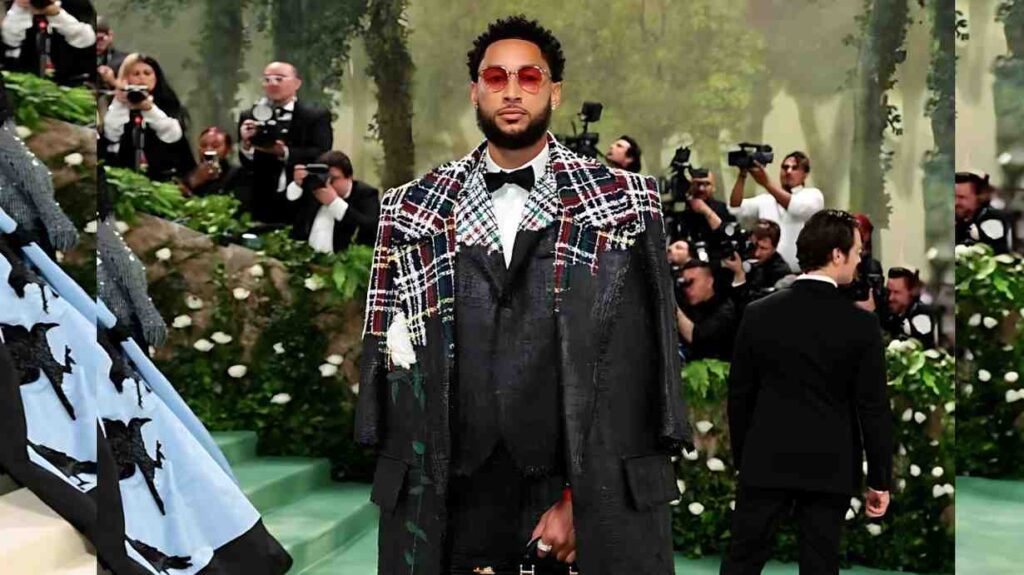 Ben Simmons with red plaid shoulders, white shirt and bow tie, red sunglasses, as photographers crowd a green gala.