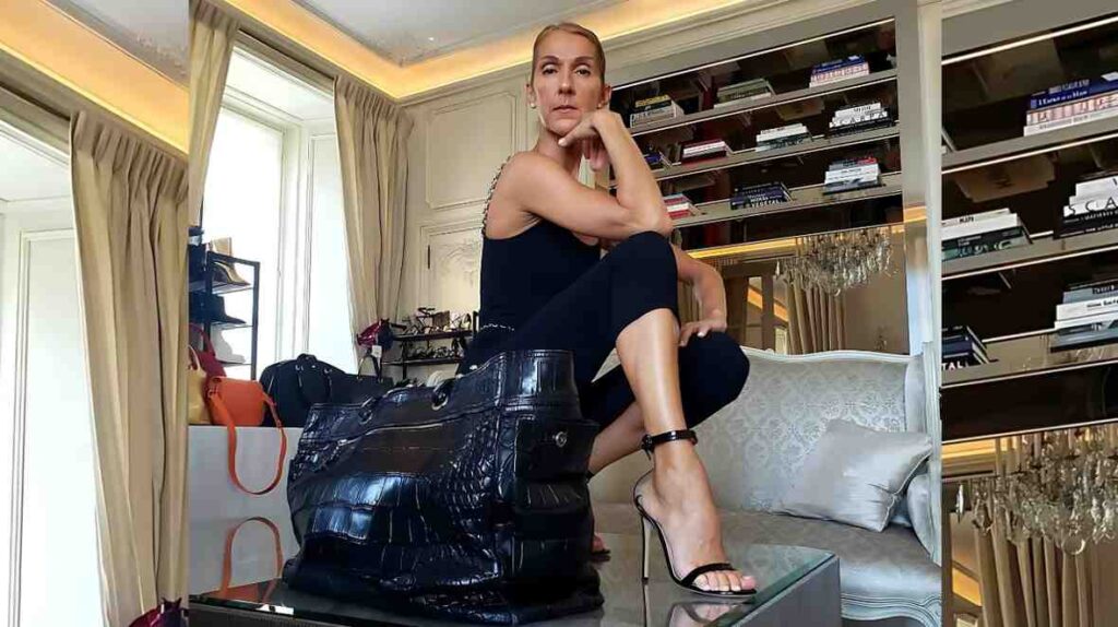 Céline Dion sits on ornate pale sofa, hand on chin, in a luxe room. A glossy black tote sits on a glass table beside her.
