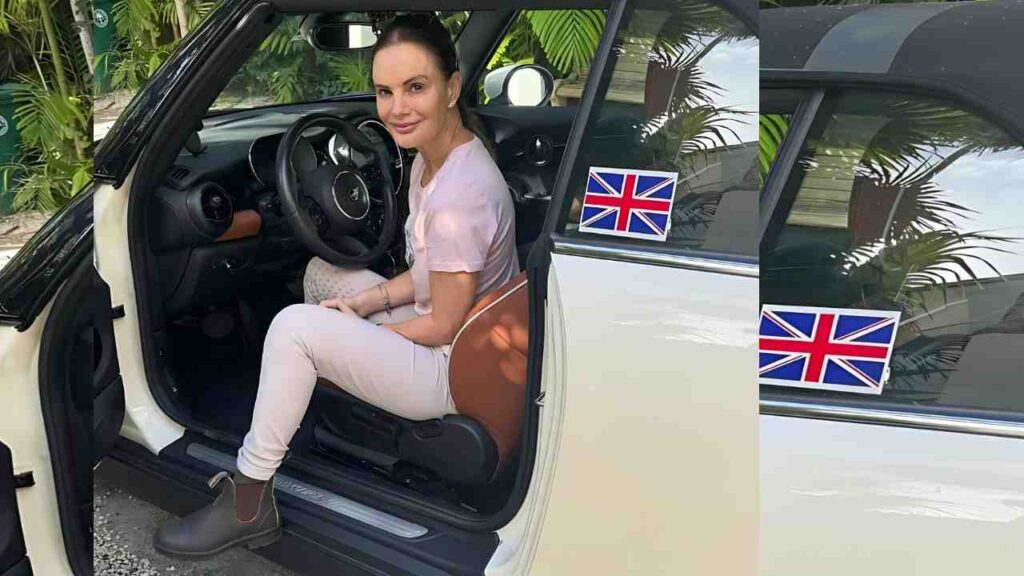 Gabrielle Anwar sits in the driver’s seat of a white car with the door open, wearing a pale pink top and white pants.